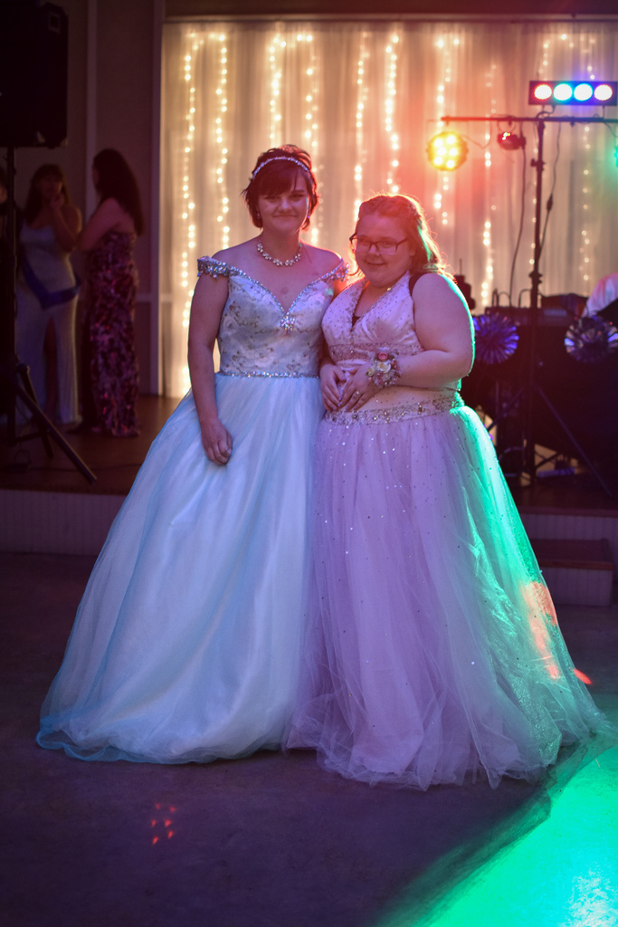 Two girls in prom dresses pose for a photo. 