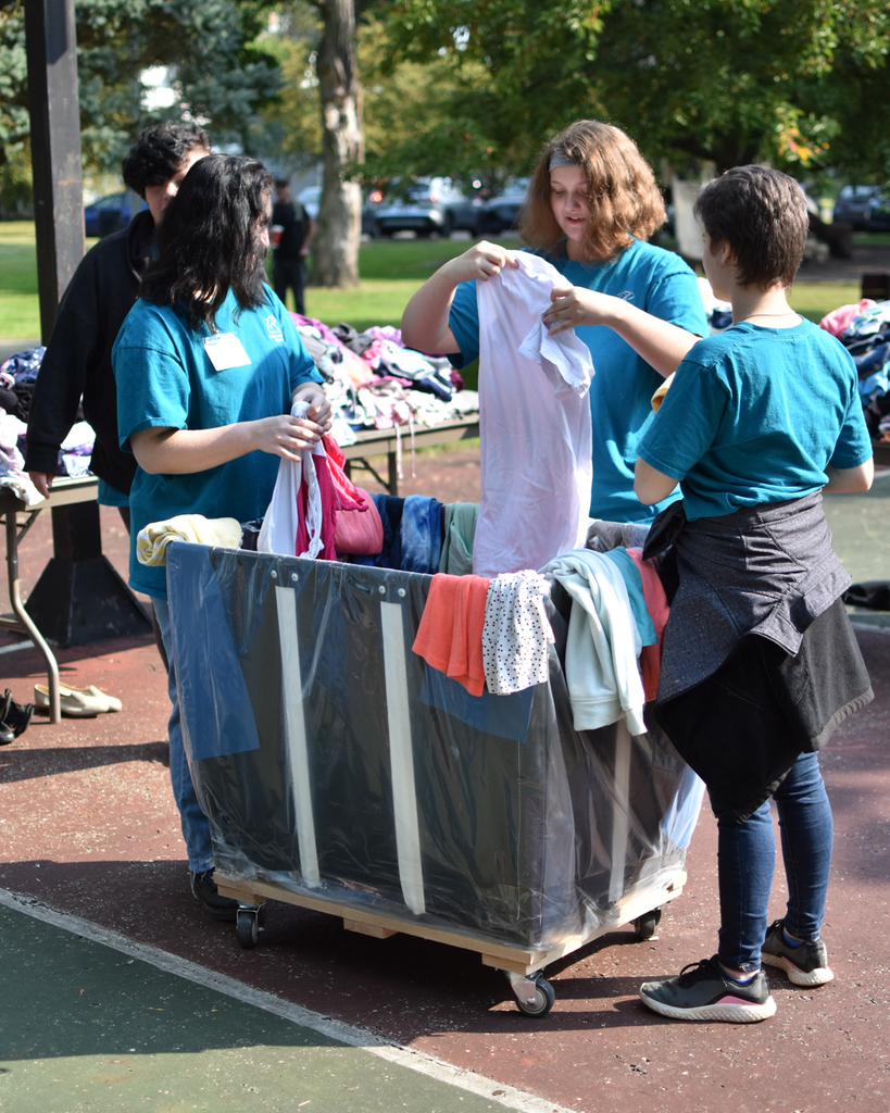three female students in teal shorts fold clothes around a rolling bin at last year's event.