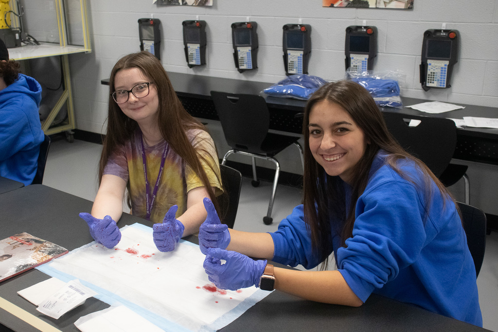 Two female students pose with thumbs up while wearing the blue latex gloves during first aid training. 