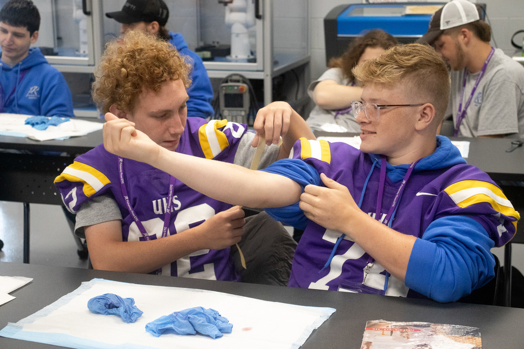 Two male students in purple football jerseys work on first aid.