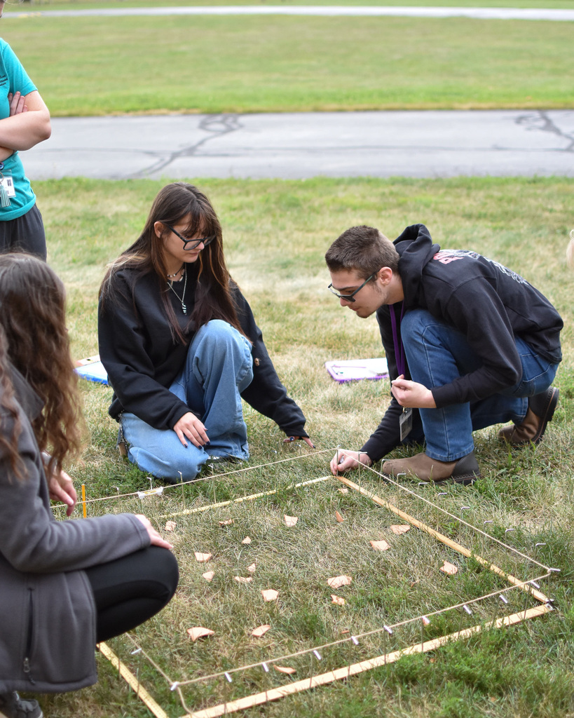 Students crouch around a square they created out of yarn and tent stakes.