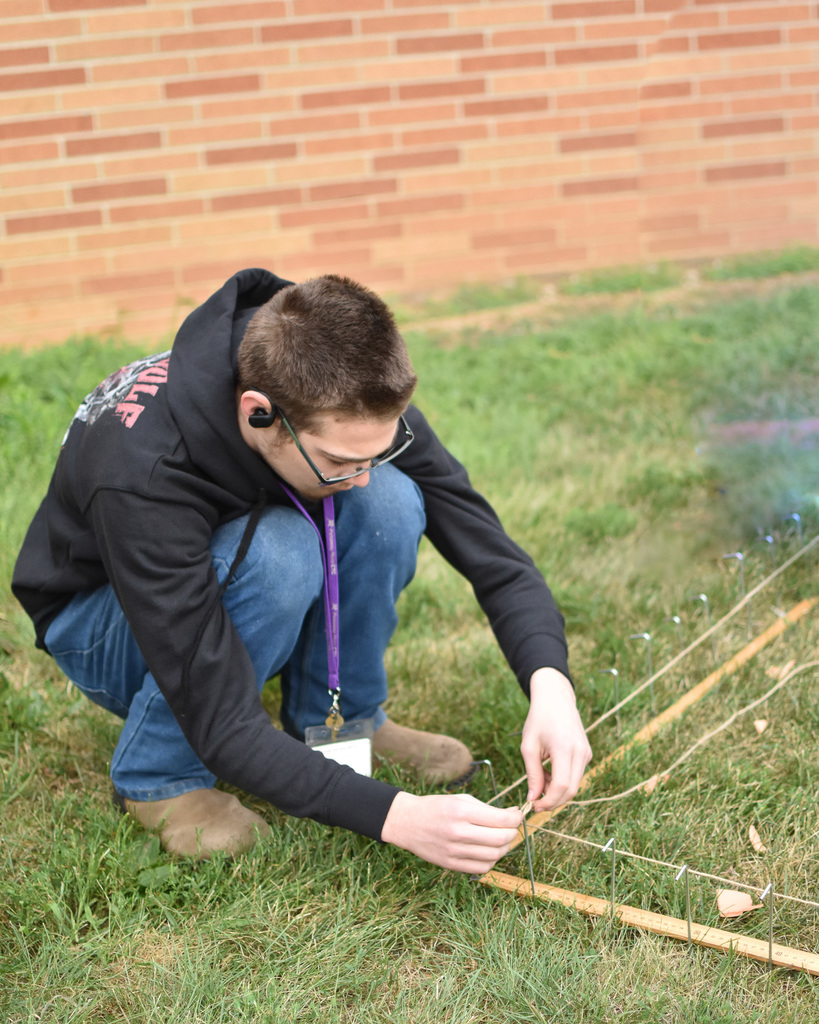 A male student kneels and ties yarn around stake.